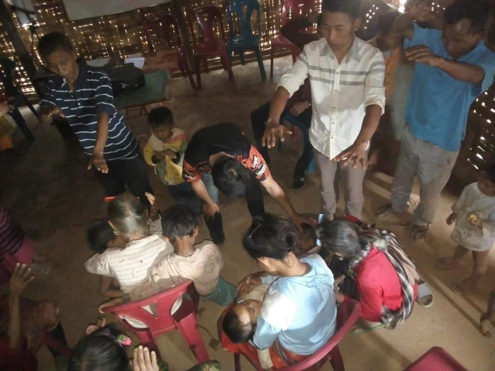A group of children and adults in a room, some seated in chairs and others standing.